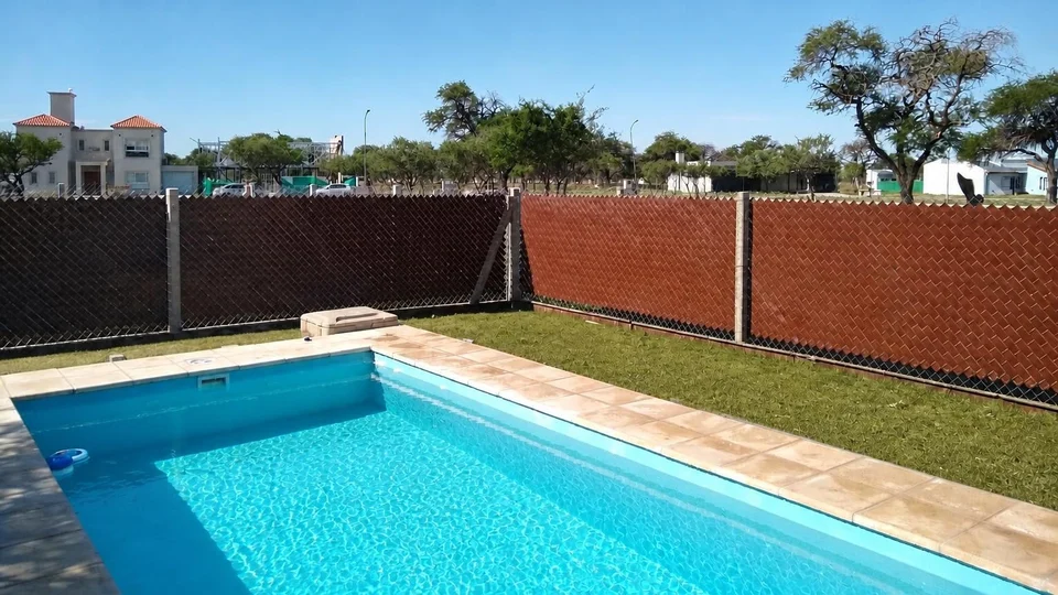 Cinta cubre cerco marrón y oscura instalada alrededor de una piscina con césped